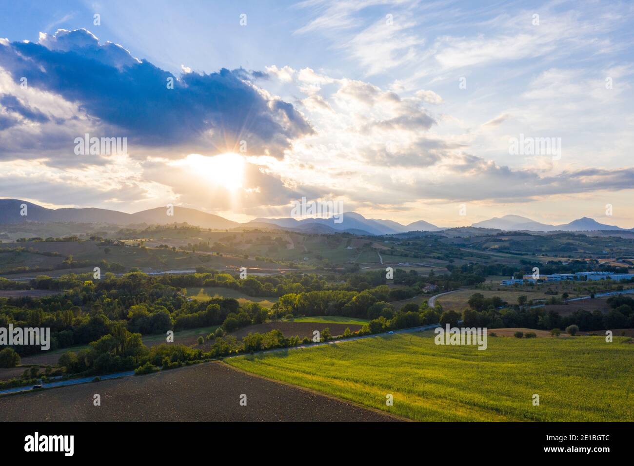 Coucher de soleil d'été pittoresque dans les collines à l'extérieur de Fabriano, Marche, Italie. Les champs verts contrastent avec les nuages bleus, le soleil est derrière les nuages Banque D'Images