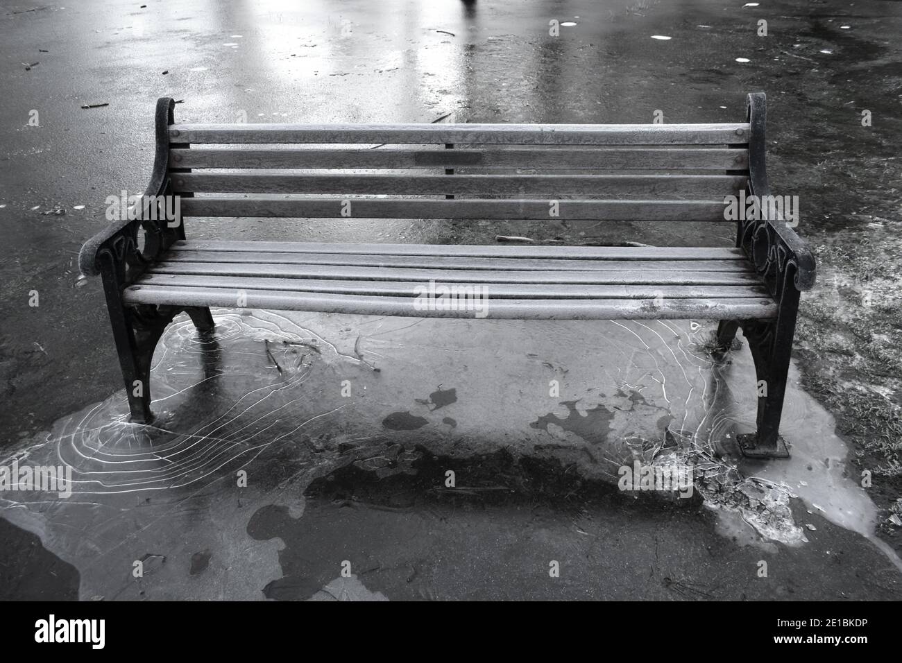 gros plan sur une image en noir et blanc d'un parc déserté banc recouvert de gel entouré d'eau gelée et solide Glace autour des jambes de banc.extérieur en hiver Banque D'Images