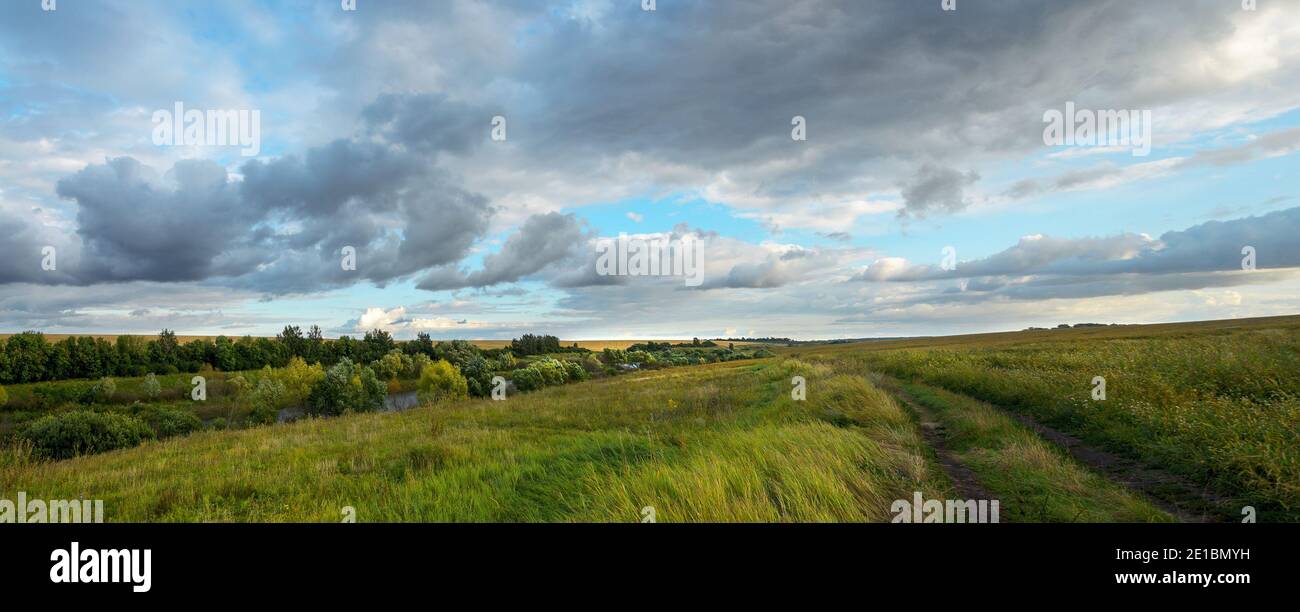 Paysage panoramique d'été avec route rurale et nuages noirs de pluie sur les champs de la ferme Banque D'Images