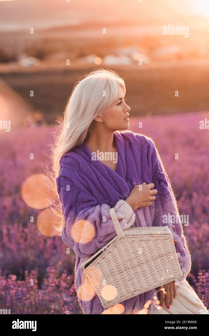 Belle femme blonde se reposant dans le champ de lavande tenant panier de paille sur coucher de soleil nature arrière-plan de gros plan. Saison Summr. Vacances. 20s. Banque D'Images