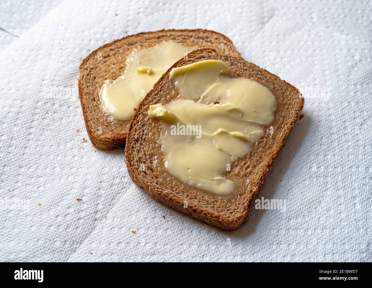 Vue de dessus de deux tranches de pain de blé légèrement grillé avec de la margarine sur des serviettes en papier blanc à la lumière naturelle. Banque D'Images