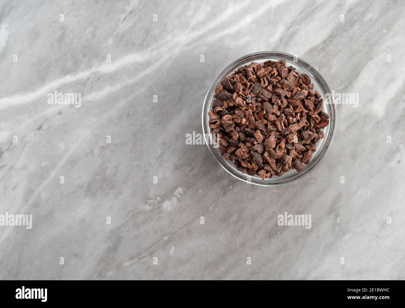 Vue de dessus d'un bol en verre rempli de nibes de cacao sur un comptoir en marbre gris éclairé par un éclairage naturel. Banque D'Images