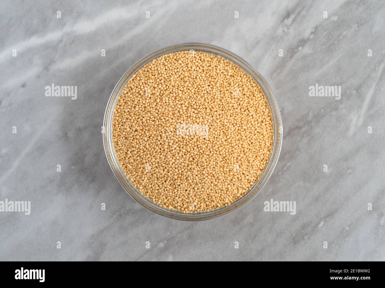Vue de dessus d'un bol en verre rempli de graines d'amaranth bio sur un comptoir en marbre gris éclairé par la lumière naturelle. Banque D'Images