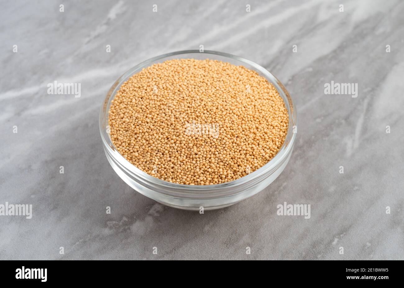 Vue latérale d'un bol en verre rempli de graines d'amaranth bio sur un comptoir en marbre gris éclairé par un éclairage naturel. Banque D'Images