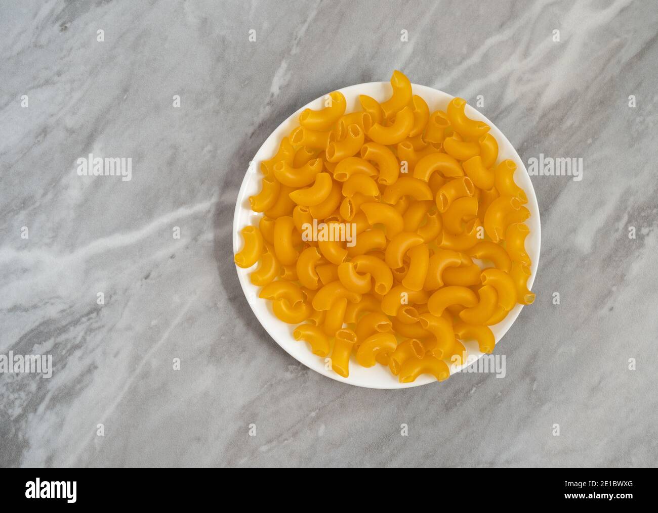 Macaroni au coude bio sur une plaque blanche au sommet d'un comptoir gris éclairé par la lumière naturelle. Banque D'Images