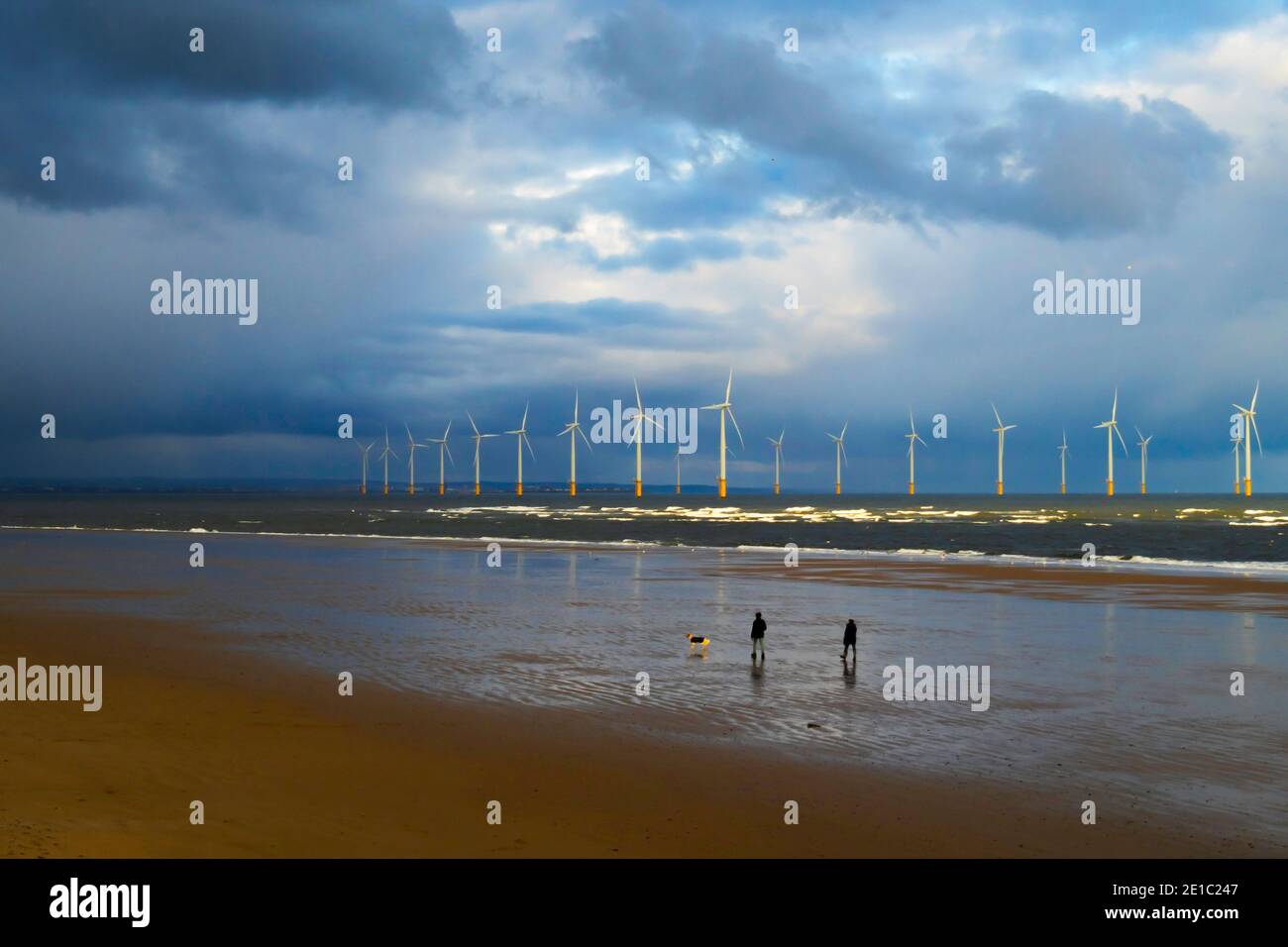 Un couple qui fait de l'exercice sur la plage un jour d'hiver ensoleillé à Coatham, Cleveland, Royaume-Uni, avec quelques-unes des éoliennes Redcar derrière des nuages noirs Banque D'Images