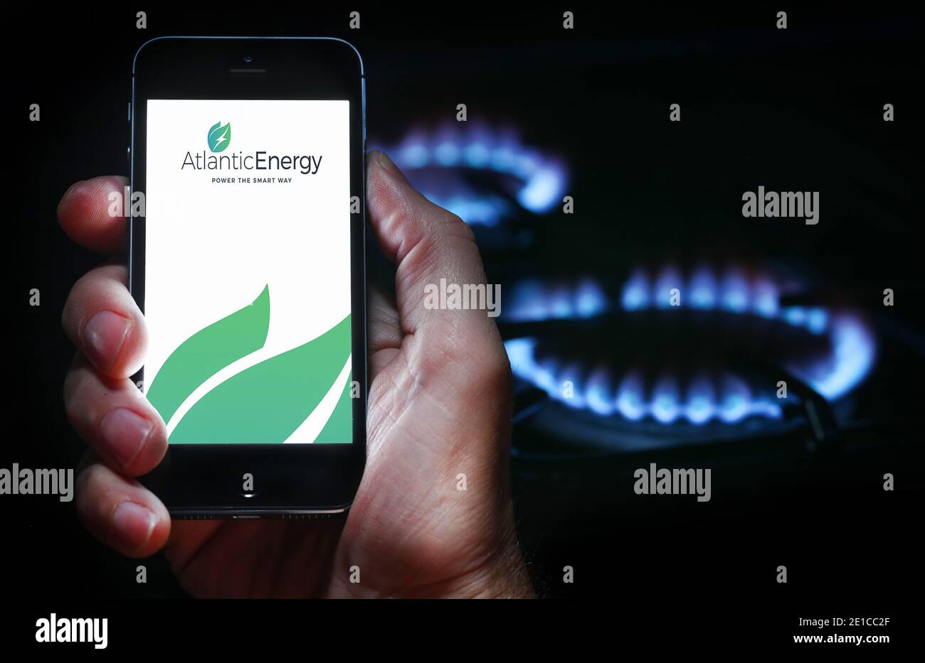 Un homme qui regarde l'application pour la compagnie d'énergie Atlantic Énergie sur son téléphone devant sa cuisinière à gaz (usage éditorial uniquement) Banque D'Images
