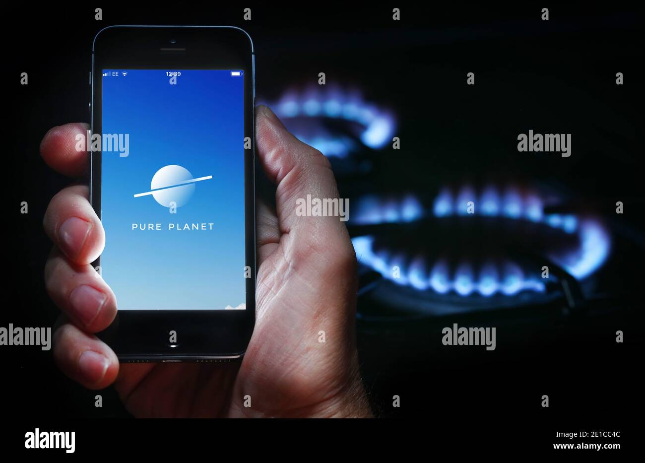 Un homme qui regarde l'application pour la société d'énergie Pure Planète sur son téléphone devant sa cuisinière à gaz (usage éditorial uniquement) Banque D'Images