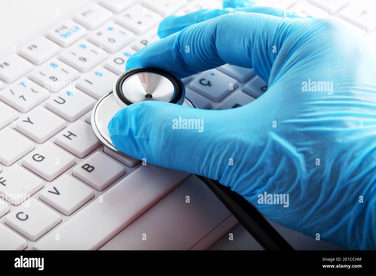 Main avec gant médical tenant un stéthoscope sur le clavier de l'ordinateur. Service de réparation informatique ou concept de diagnostic de l'état de santé des pc. Banque D'Images