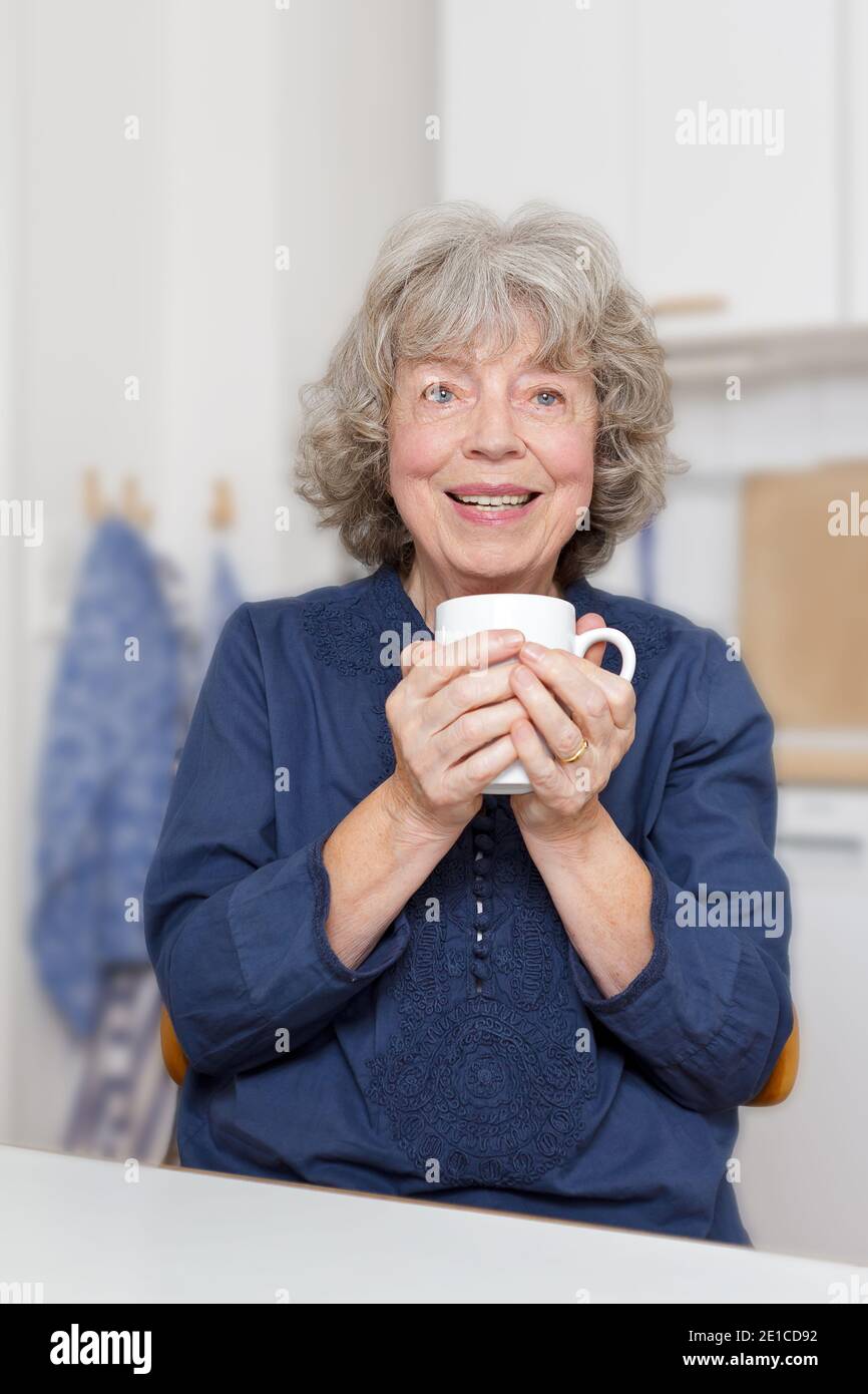 Portrait d'une femme âgée souriante à sa table de cuisine avec une tasse Banque D'Images