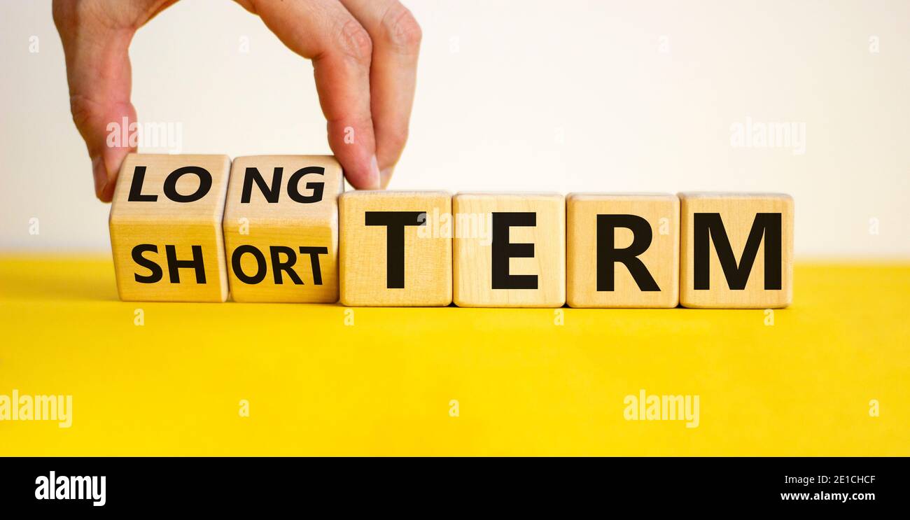 Symbole à long terme ou à court terme. La main tourne les cubes et change  les mots 'court terme' en 'long terme'. Belle table jaune, fond blanc.  Affaires et long Photo Stock -