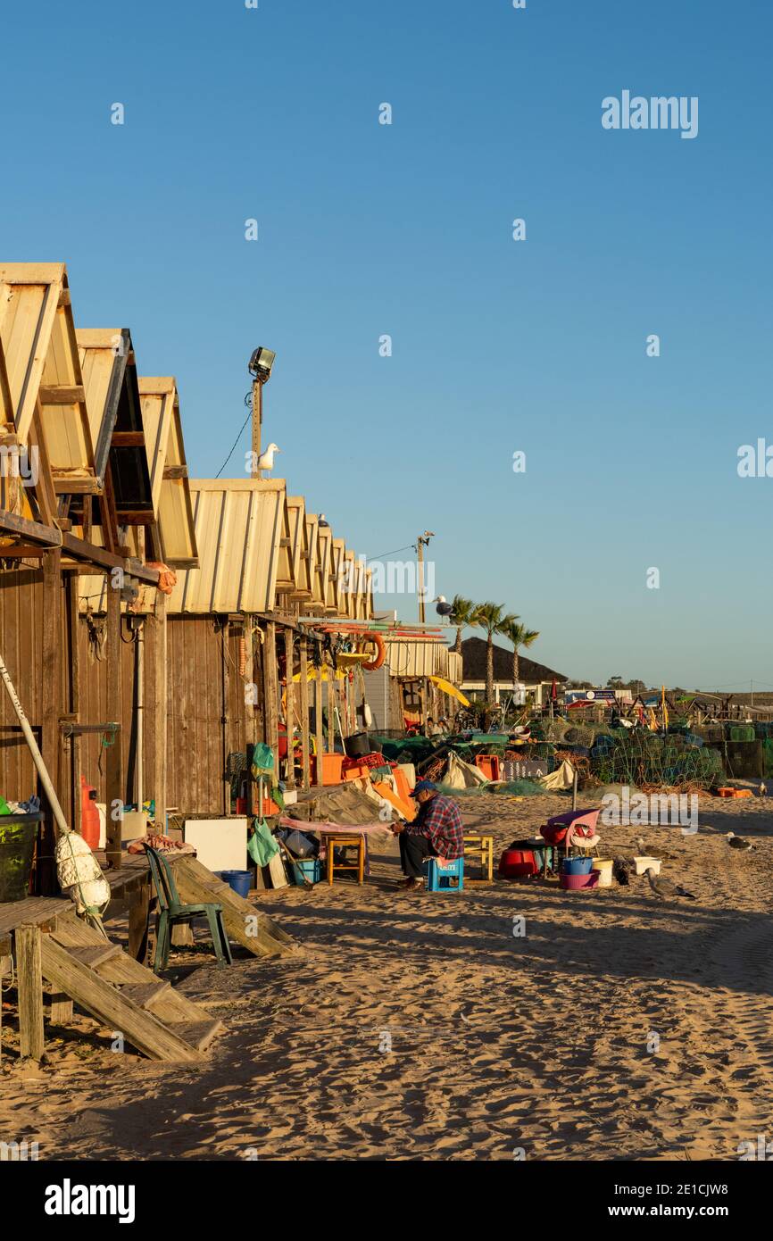 Amaraco da Pera, Portugal - 30 décembre 2020 : fiserman assis à l'extérieur de sa hutte au coucher du soleil et en train de réparer ses filets Banque D'Images