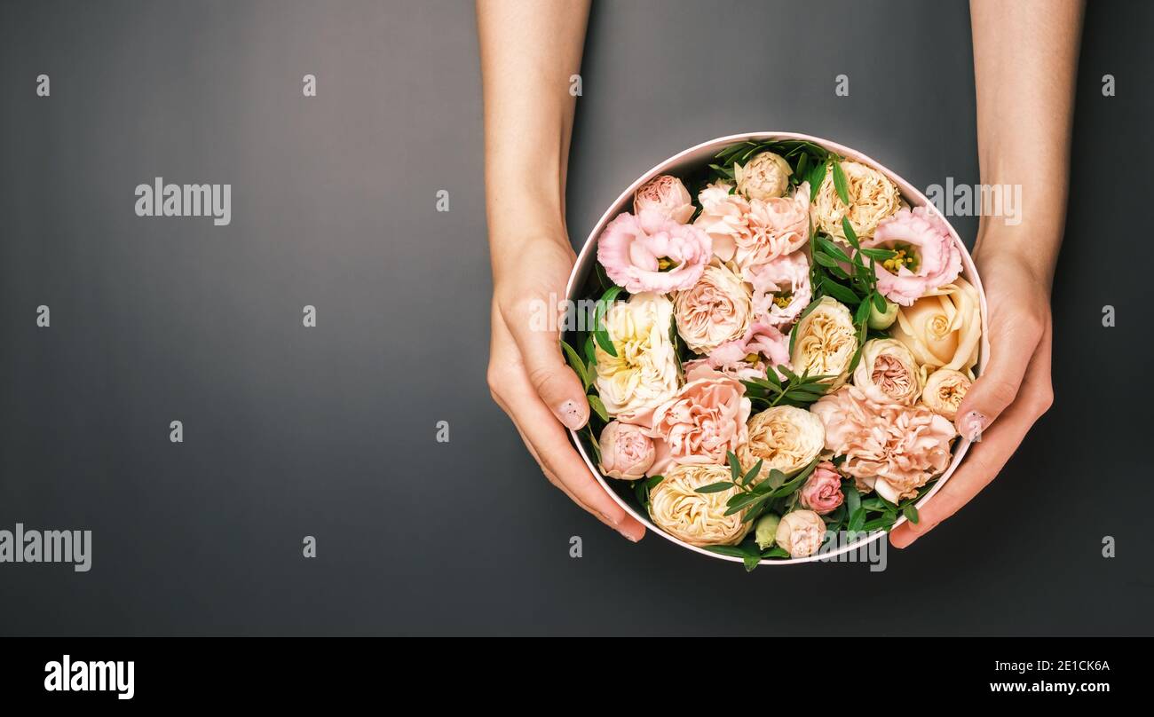 Boîte cadeau rose avec composition florale dans les mains des femmes sur le fond noir avec espace de copie. Cadeau pour la Saint-Valentin, International Women's Banque D'Images