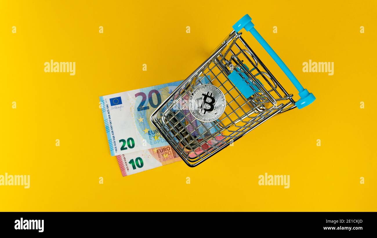 Bitcoin à l'intérieur d'un petit chariot à provisions et billets en euros sur fond jaune arrière-plan,vue aérienne Banque D'Images