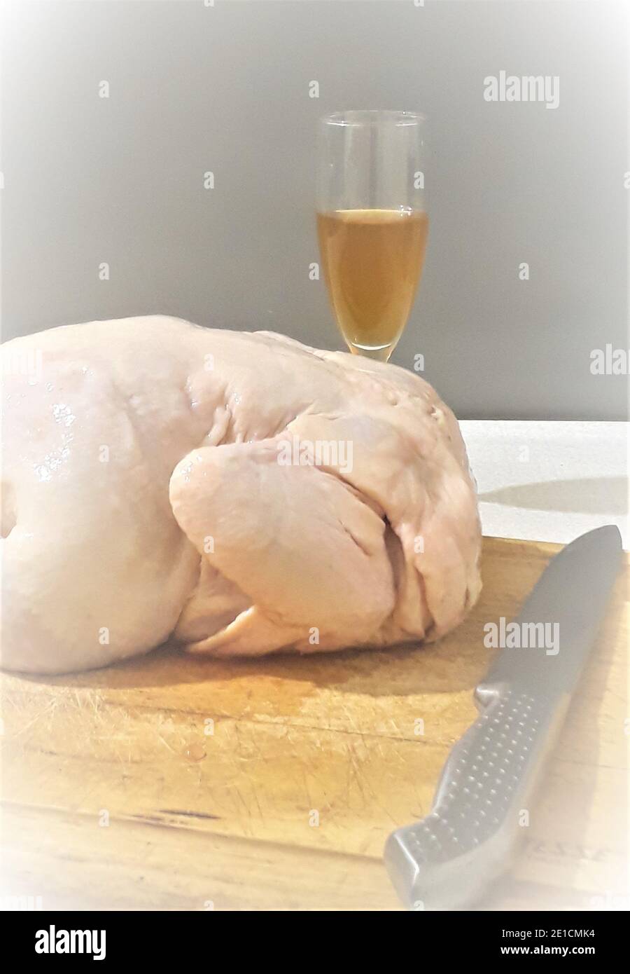 La carcasse de poulet repose sur une vieille planche à découper en bois sur le fond d'un réfrigérateur gris. Sur la carte se trouve un couteau en métal, derrière le réfrigérateur se trouve un verre de vin Banque D'Images