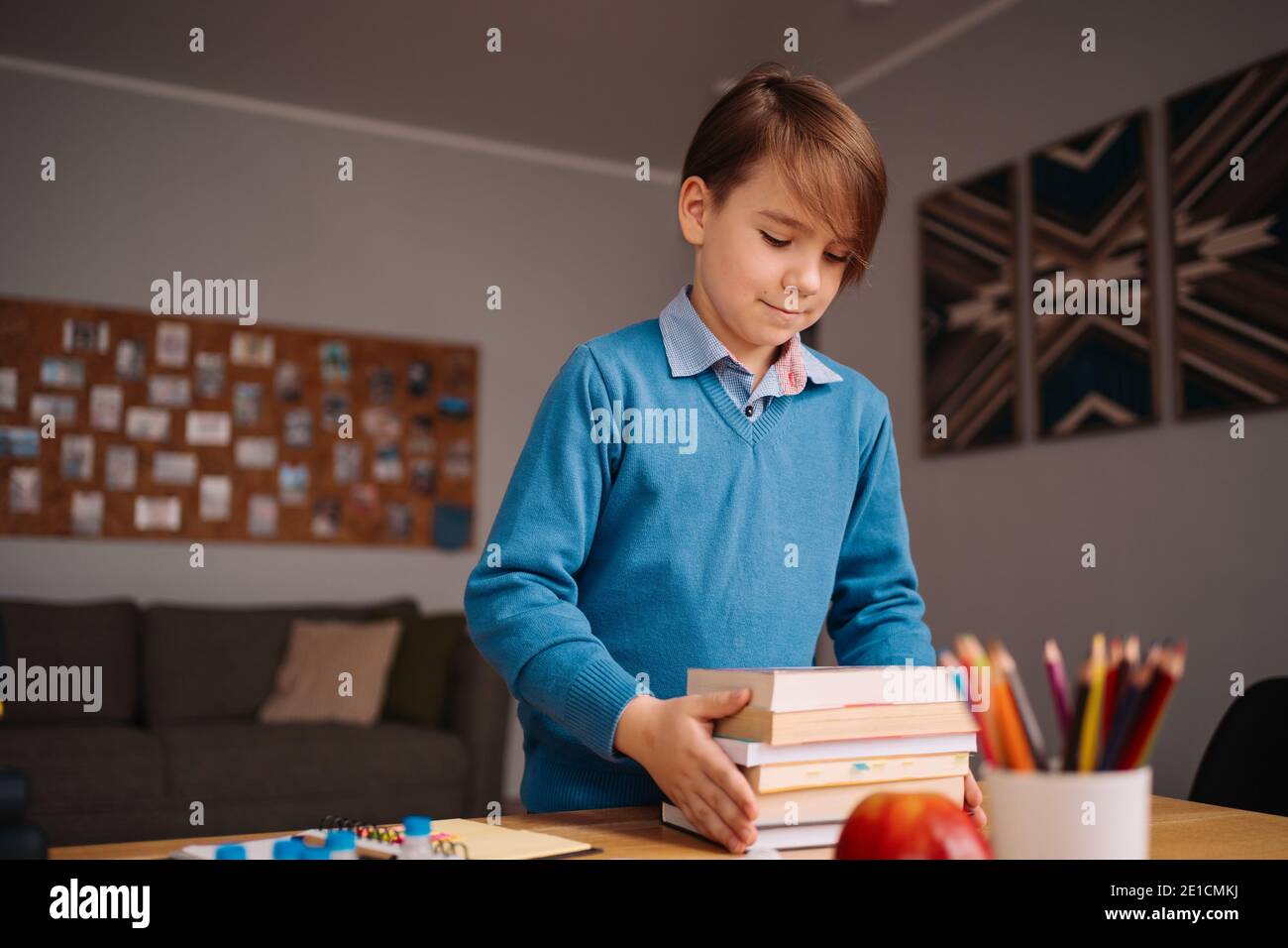 Formation en ligne à distance, apprentissage sur Internet. Garçon de première classe étudiant à la maison, tenant un tas de livres, se préparer pour la leçon en ligne Banque D'Images