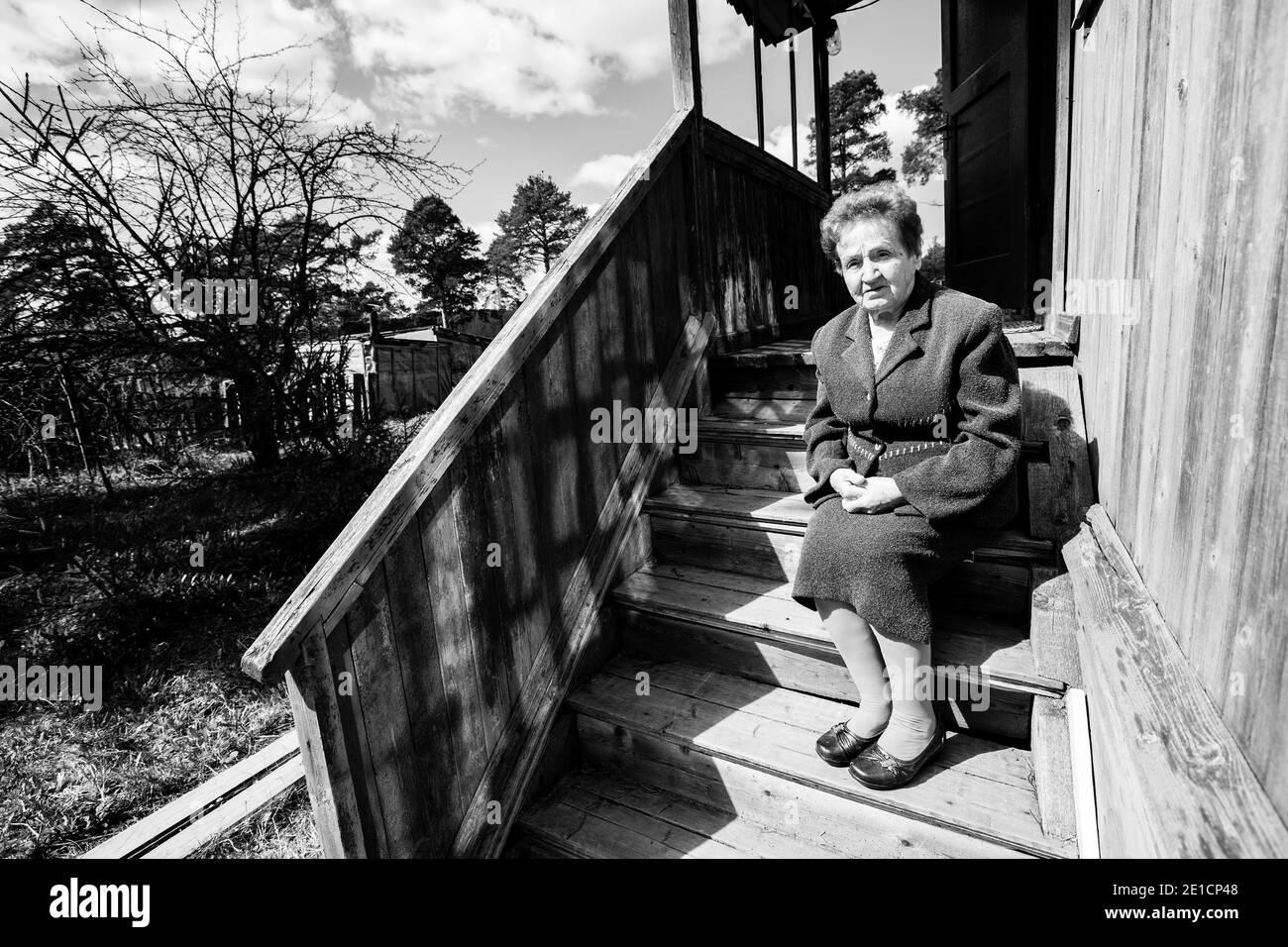 Une vieille femme assise sur le porche de la maison. Photo en noir et blanc. Banque D'Images