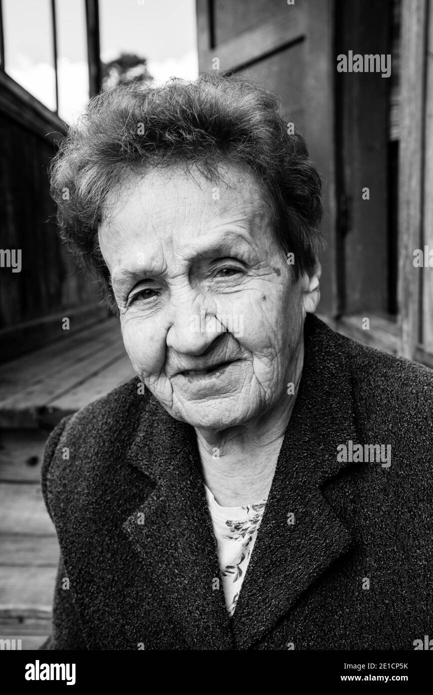 Une vieille femme près d'une maison rurale. Photo en noir et blanc. Banque D'Images