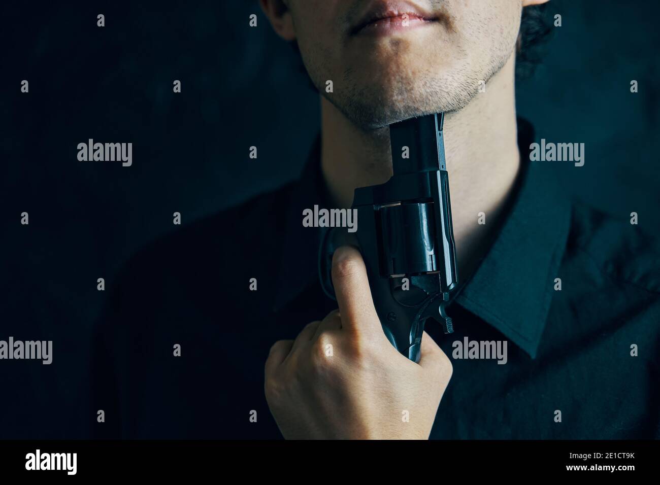 Guy avec un fusil se prépare à commettre le suicide. Personne en chemise noire museau de fusil au menton. Dépression avec issue fatale. Banque D'Images