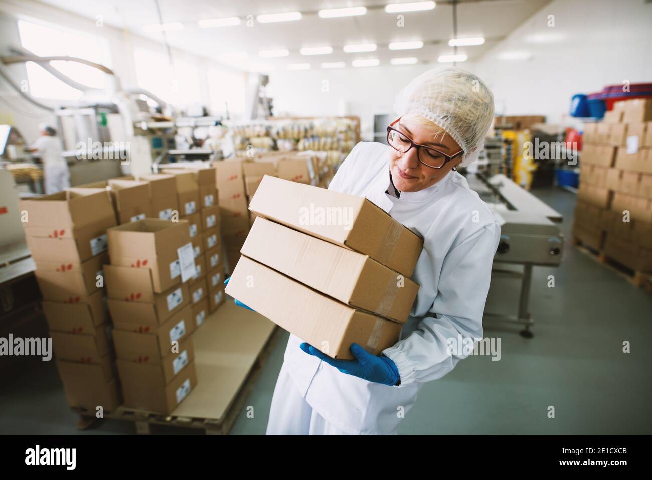 Une employée de vêtements stériles soulève des boîtes lourdes en usine. Banque D'Images