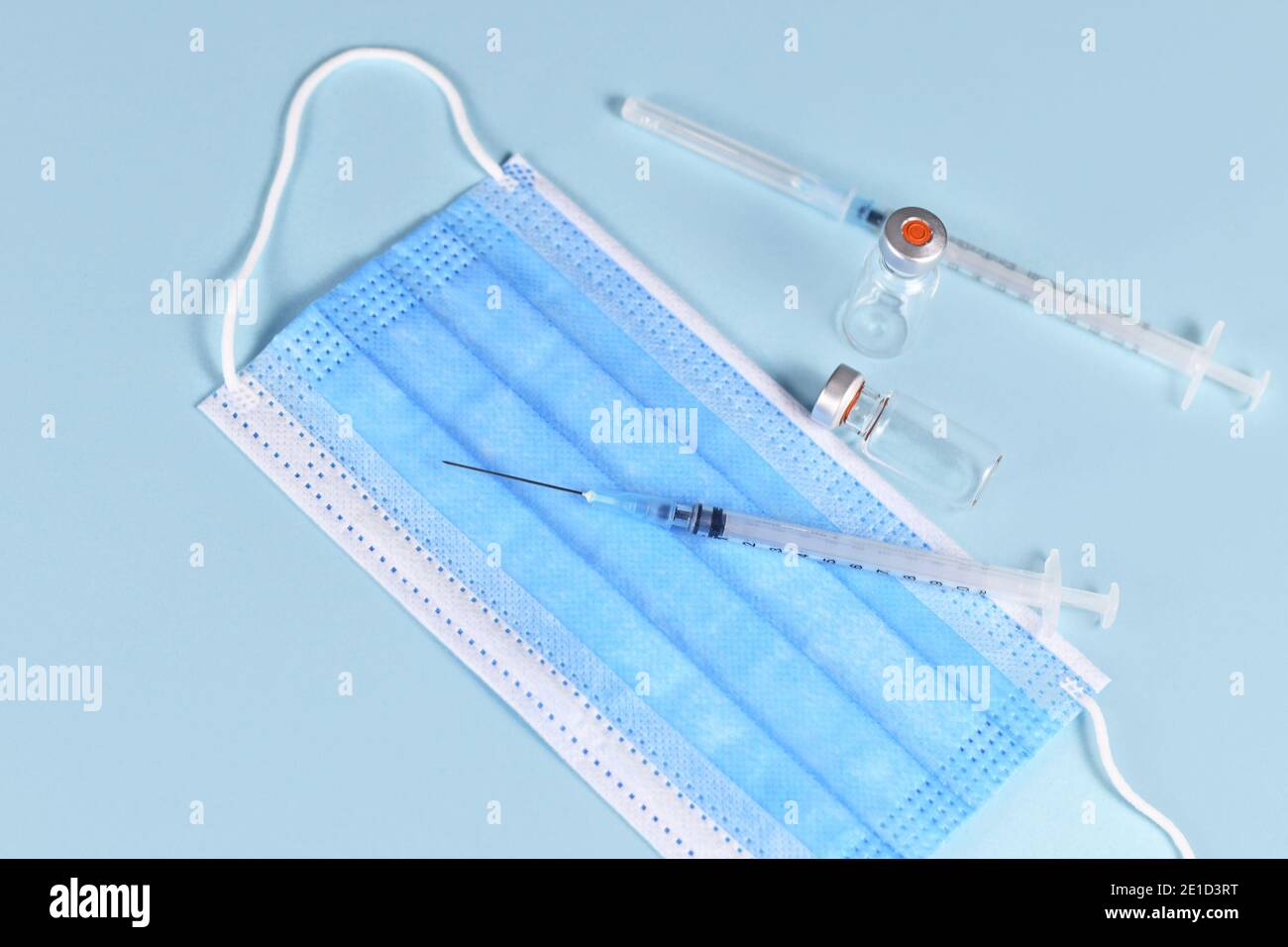 Vaccin contre le coronavirus concept avec seringue, masque facial et flacons sur fond bleu Banque D'Images