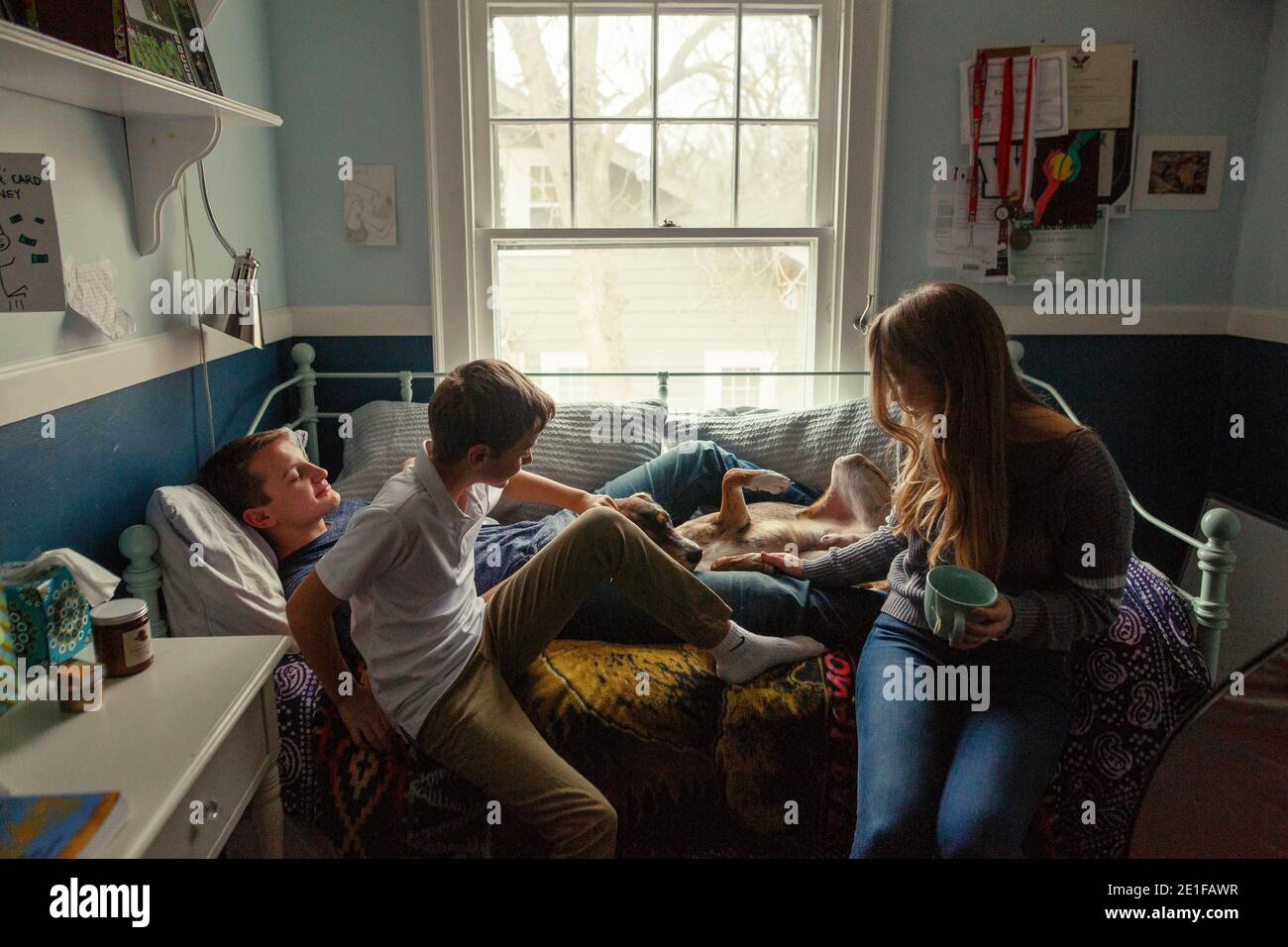 trois frères et sœurs s'assoient sur un lit en forme de cuddling avec un mignon chien de famille dans la chambre Banque D'Images