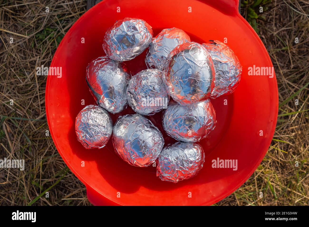 Pommes de terre pour cuire au feu, enveloppées dans du papier d'aluminium, allongées dans une tasse rouge. Alimentation, alimentation saine. Cuisson au charbon de bois ou au feu. Dîner de camping extérieur à natur Banque D'Images