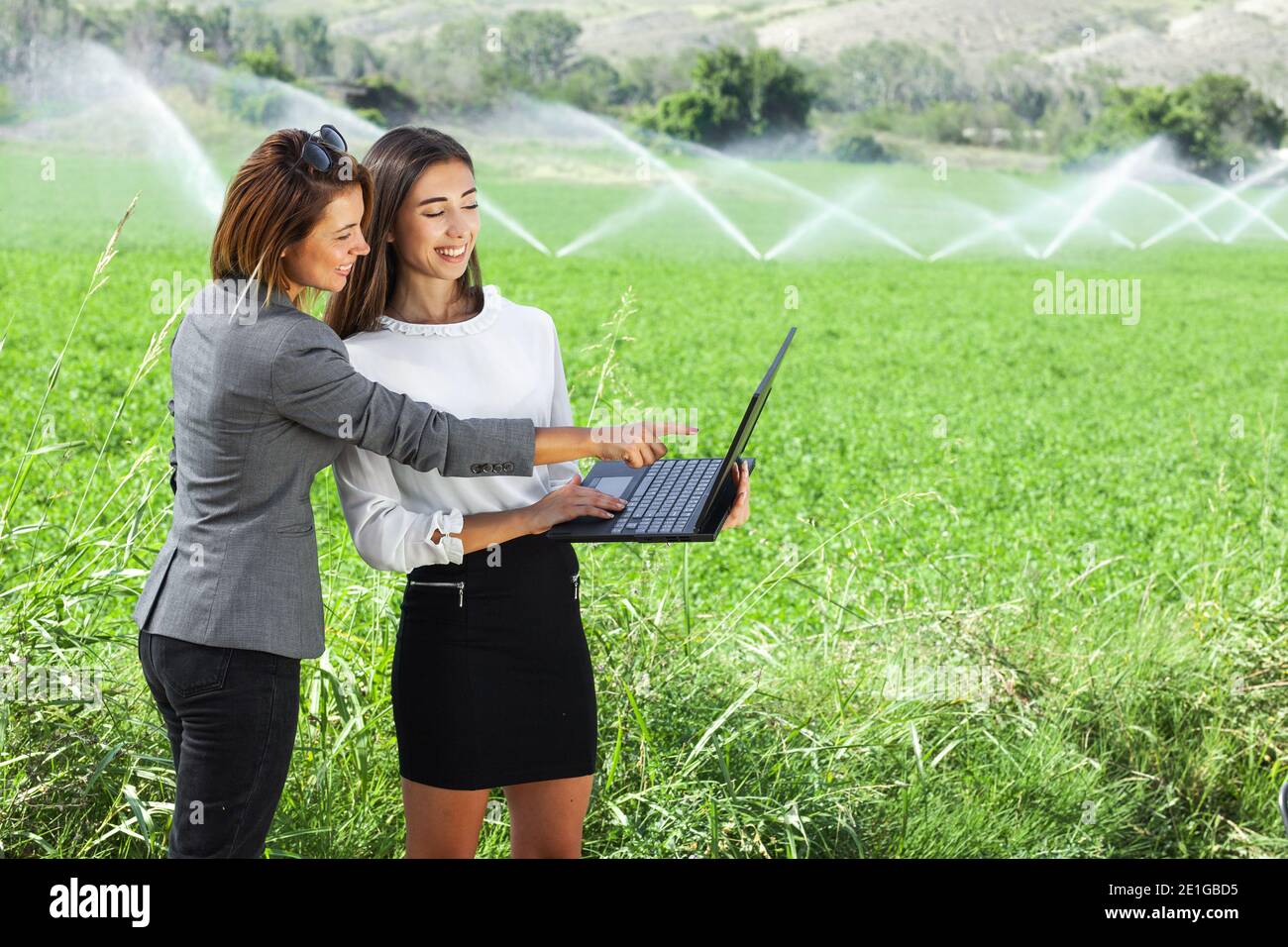 Femmes d'affaires avec un ordinateur portable dans un champ avec système d'irrigation agricole. Arroseurs d'eau en arrière-plan. Banque D'Images