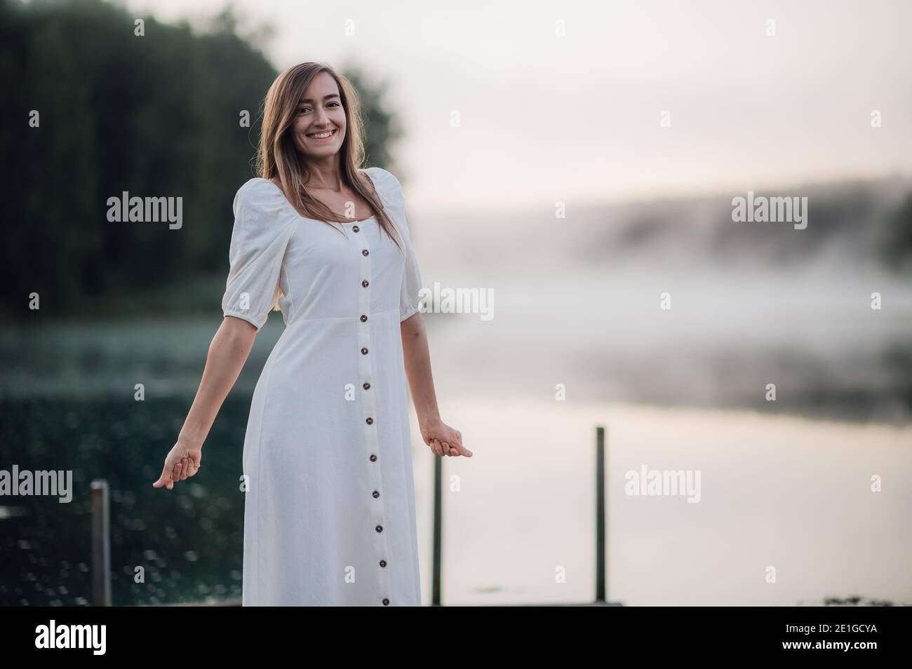Une femme heureuse vêtue de blanc aime le matin sur un lac. Le brouillard flotte sur l'eau. Banque D'Images