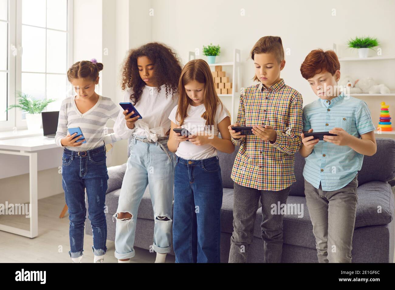 Groupe d'enfants de race mixte debout et jouant ou bavardant sur les smartphones Banque D'Images