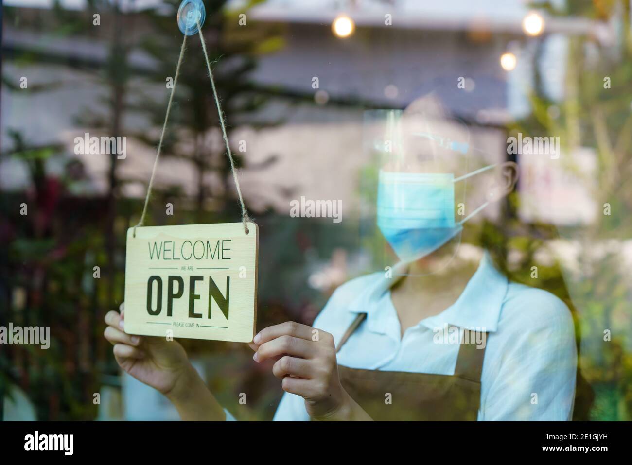 La propriétaire d'entreprise asiatique femme porte un masque de protection et un masque de protection pour le visage suspendu panneau ouvert à son restaurant / café, ouvert à nouveau après verrouillage pour nouveau NOR Banque D'Images