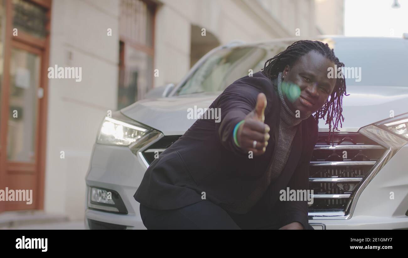 Homme d'affaires noir debout devant la nouvelle voiture et montrant le pouce vers le haut. Acheter une nouvelle voiture. Photo de haute qualité Banque D'Images