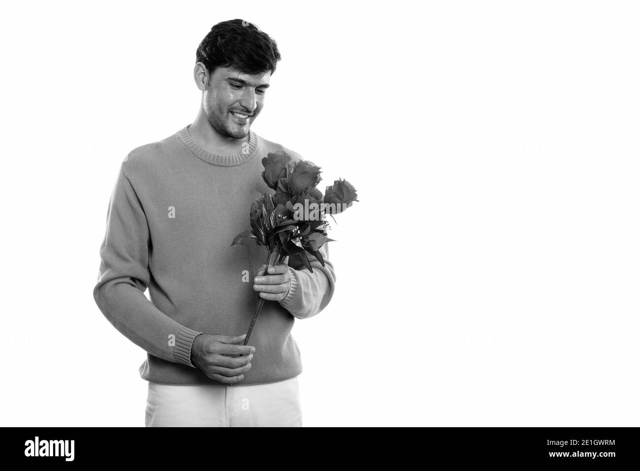 Studio shot of young man smiling persan heureux tout en maintenant et en regardant les roses rouges prête pour la Saint-Valentin Banque D'Images