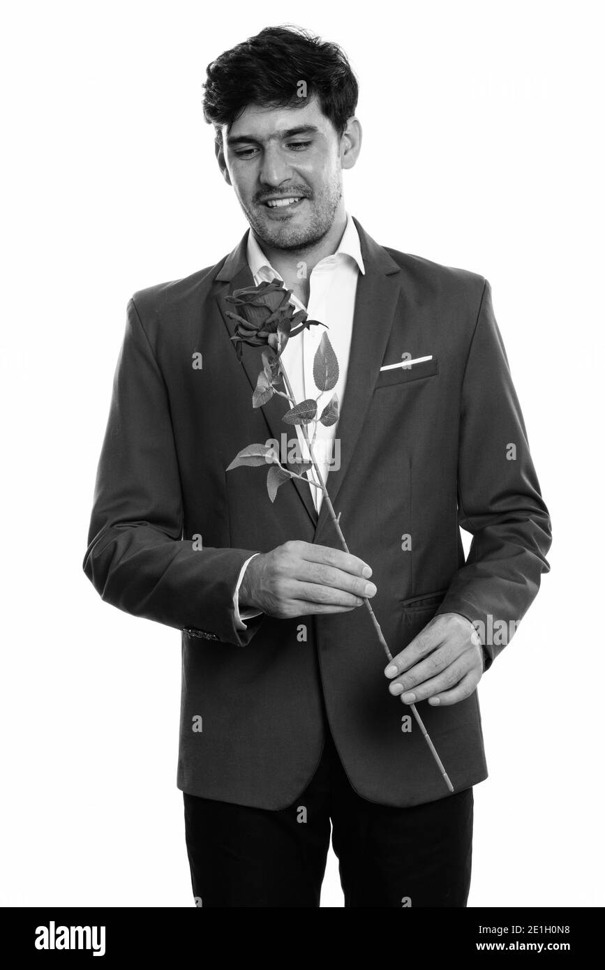 Studio shot of young businessman smiling persan heureux tout en maintenant et en regardant rose rouge Banque D'Images