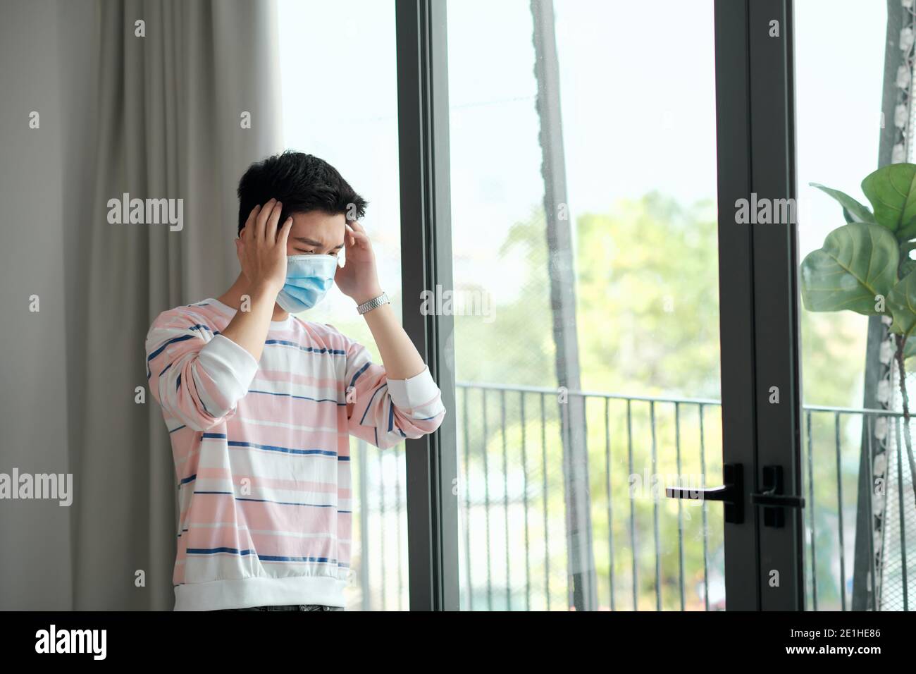 COVID-19. Homme malade de coronavirus regardant par la fenêtre et portant un masque de protection et de récupération de la maladie à la maison. Banque D'Images