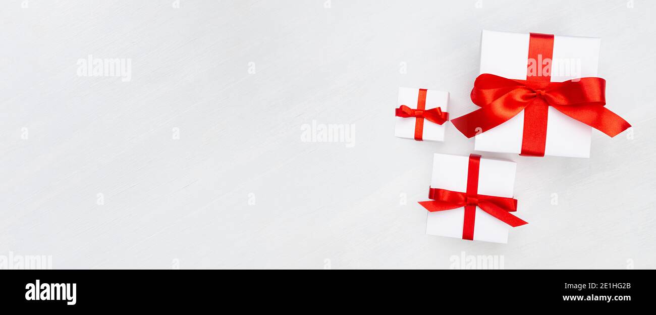 Élégantes boîtes cadeaux blanches classiques de fête avec noeud rouge, ruban sur panneau de bois blanc comme bannière, arrière-plan pour le design commercial. Banque D'Images