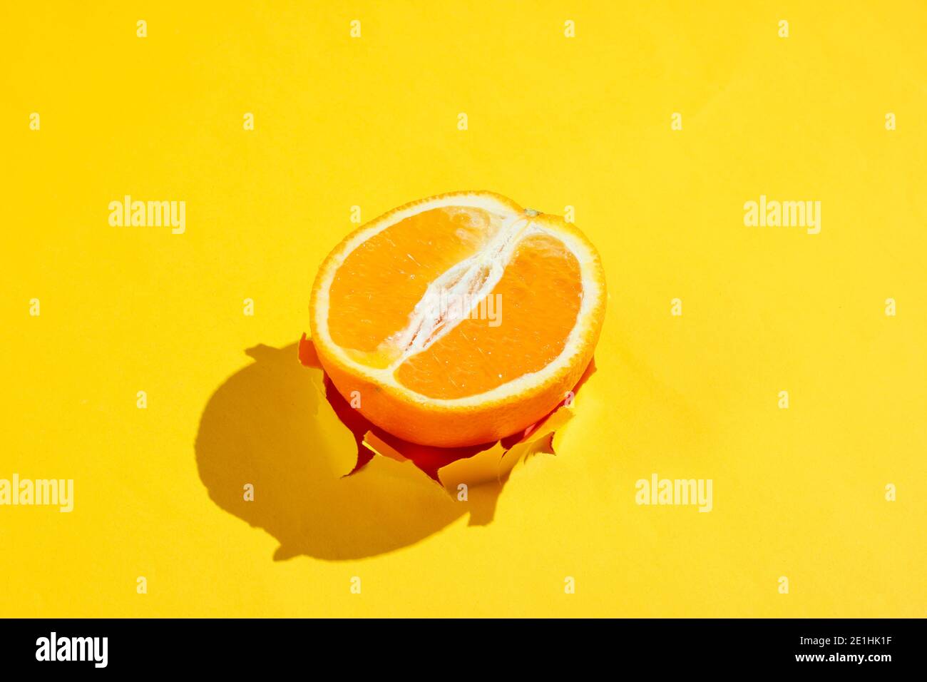 Moitié orange dans le trou déchiré du papier jaune. Concept de fruit minimaliste Banque D'Images