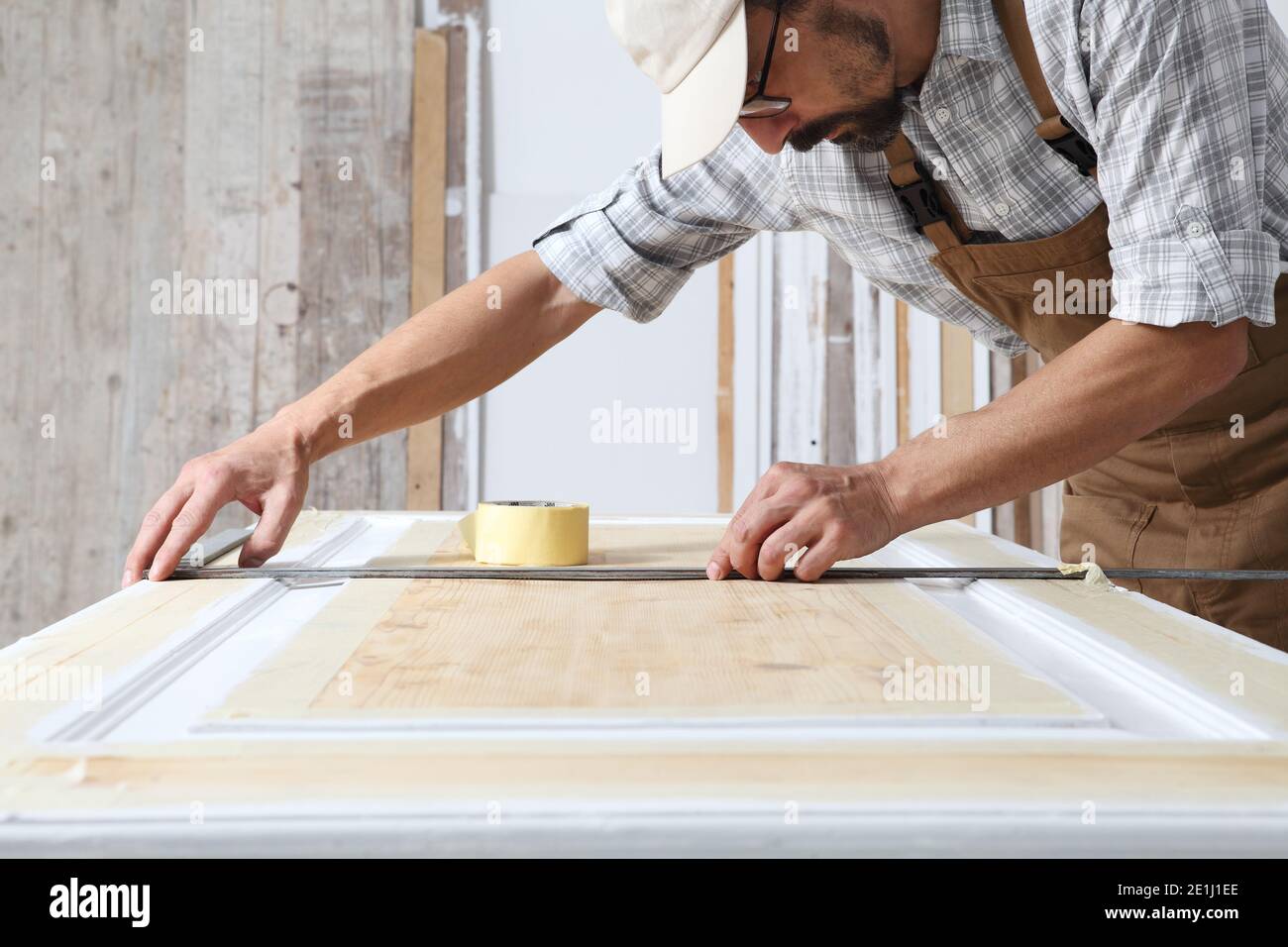 Menuisier mâle travaillant le bois dans l'atelier de menuiserie, prenant des mesures sur la porte en bois avec une règle carrée en métal sur une porte en bois, portant l'ensemble et Banque D'Images