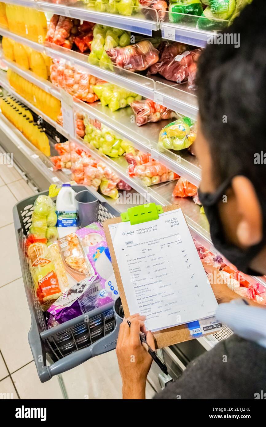 Cape Town, Afrique du Sud - 10 décembre 2020 : membre du personnel qui cueille les produits d'épicerie de l'étagère pour un service de livraison express à domicile au service local Pick n Pay su Banque D'Images