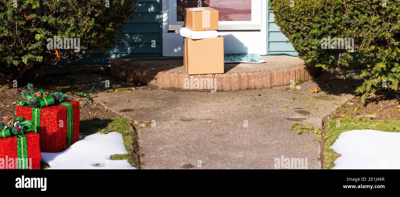Neige sur le sol à côté des décorations des fêtes de Noël avec des paquets livrés au stoop avant. Banque D'Images