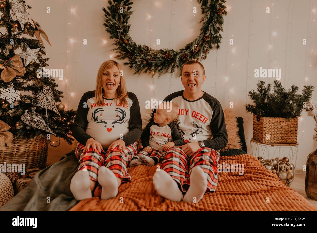 joyeux famille en pyjama avec enfant assis sur le lit dans la chambre. les parents montrent des langues. vêtements pour la nouvelle année style ensembles. Saint-Valentin ce Banque D'Images