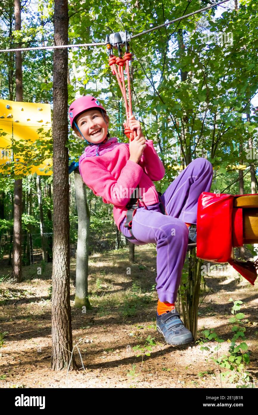 Jeune fille sur une ligne de fermeture éclair entre les arbres dans un parc d'aventure pour enfants. Banque D'Images