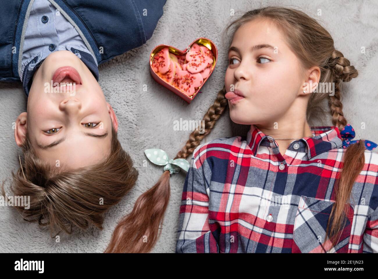 Drôle de soeur et de frère bâton de langues à l'autre, heureux et souriant des adolescents avec des biscuits en forme de coeur Banque D'Images