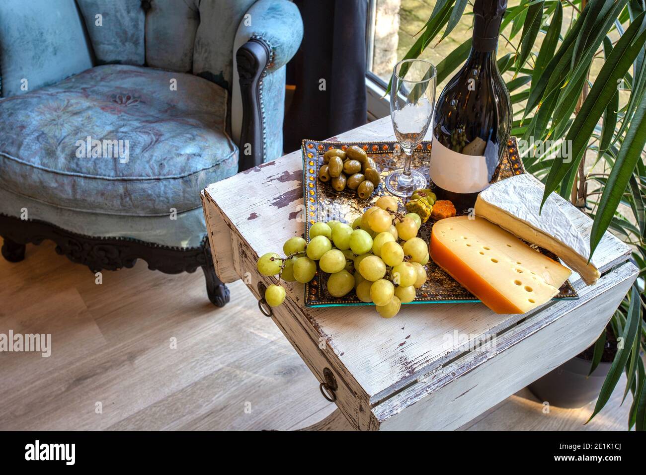 plateau de fromages avec raisins et vin sur une table près d'une fenêtre avec une chaise confortable. Décoration intérieure moderne Banque D'Images