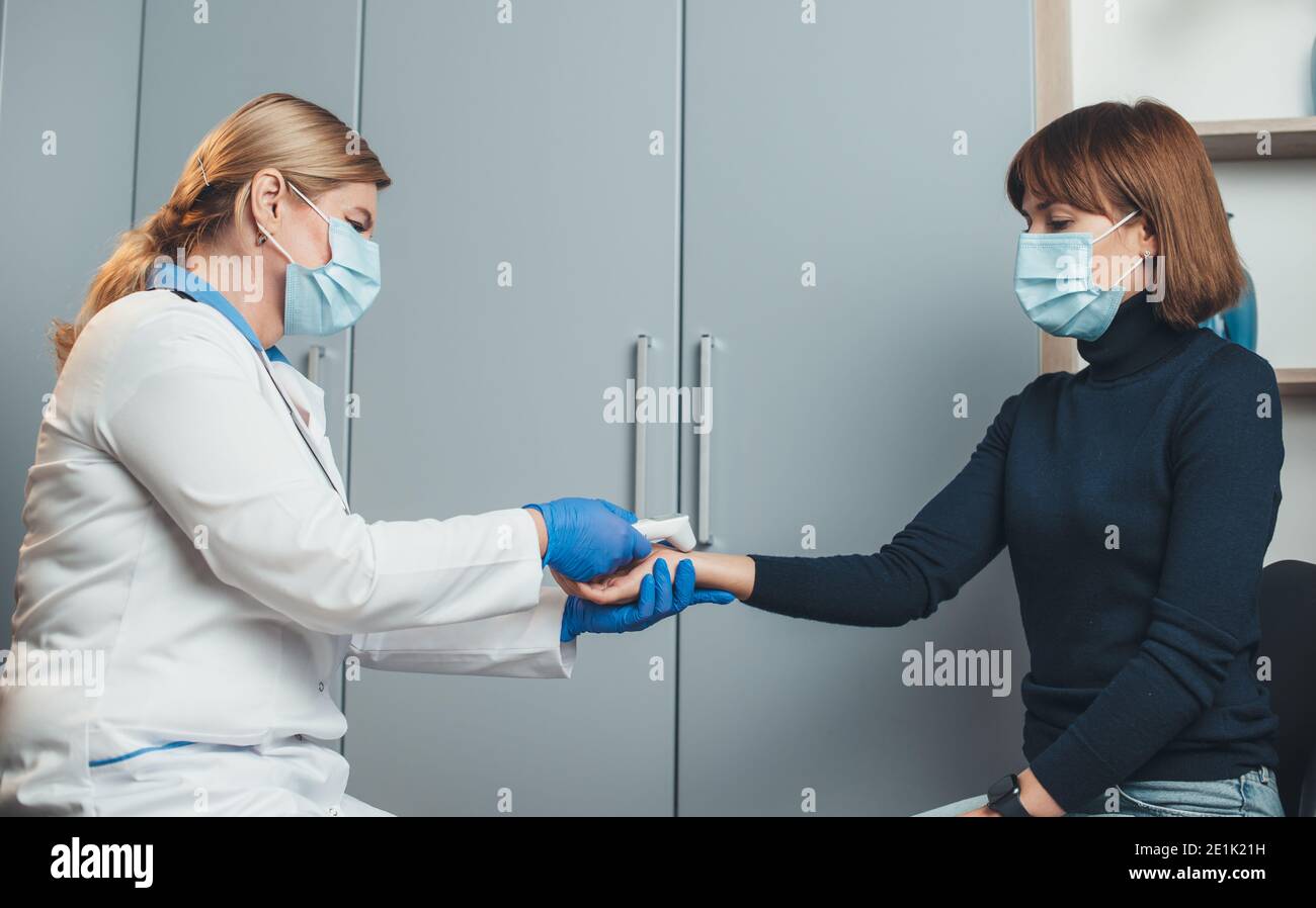 Le médecin blond senior mesure la température sur la main du patient à l'aide d'un thermomètre électrique au bureau de travail Banque D'Images