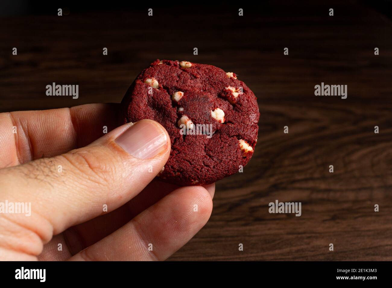 Main tenant un cookie en velours rouge avec du chocolat blanc. Banque D'Images
