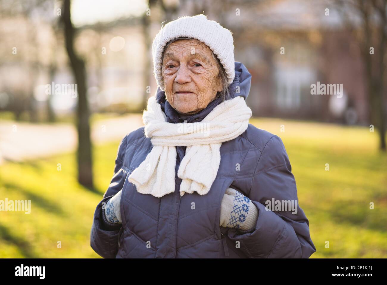 Joyeuse femme mature exprimant des émotions positives en hiver tricoté  chapeau blanc et écharpe en manteau bleu dans le parc de la ville. Femme  âgée saison froide dehors. EXC Photo Stock -