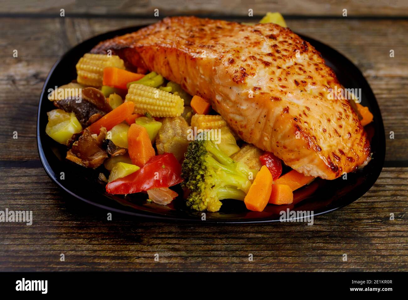 Un morceau de saumon cuit avec des légumes asiatiques sautés sur une assiette noire. Gros plan. Banque D'Images
