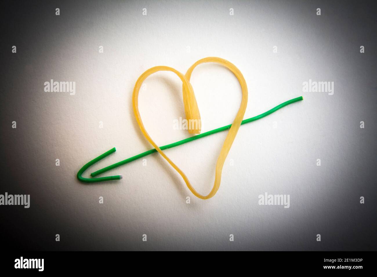 Forme de coeur créative faite à partir d'un élastique jaune et fil vert placé sur un fond blanc Banque D'Images