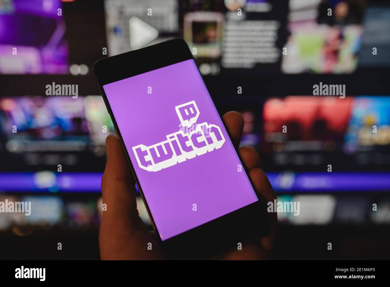 Homme tenant un smartphone avec le logo Twitch devant le site officiel Banque D'Images